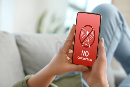 Woman holding mobile phone with text NO CONNECTION on screen at home