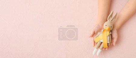 Téléchargez les photos : Hands with toy and golden ribbon on beige background with space for text. Childhood cancer awareness concept - en image libre de droit