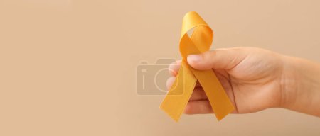 Téléchargez les photos : Hand with golden ribbon on beige background. Childhood cancer awareness concept - en image libre de droit
