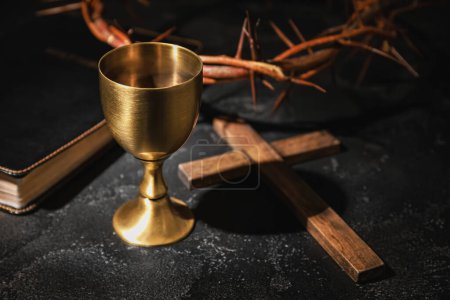 Wine cup, crown of thorns, cross and Holy Bible on dark background, closeup