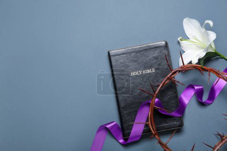 Heilige Bibel mit lila Schleife, Dornenkrone und Lilienblüte auf blauem Hintergrund. Karfreitagskonzept
