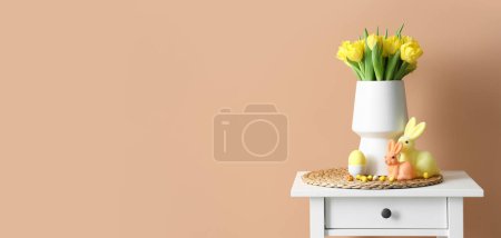 Foto de Jarrón con tulipanes amarillos, huevos de Pascua y conejos en la mesa cerca de la pared beige. Banner para el diseño - Imagen libre de derechos