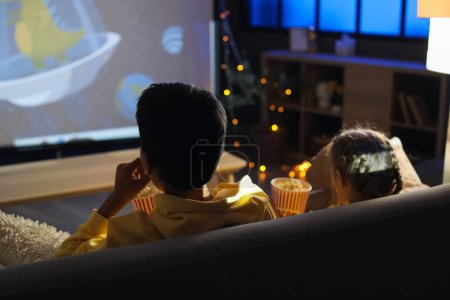Little boy and his sister with popcorn watching cartoons on projector screen at home