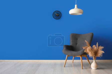 Foto de Elegante sillón gris, lámpara, reloj y jarrón con hierba de pampas cerca de la pared azul - Imagen libre de derechos