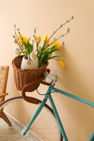 Bicycle with tree branches, Easter eggs and tulips near beige wall, closeup