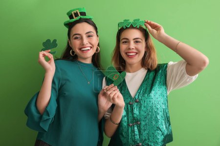 Foto de Young women with paper clover and hat on green background. St. Patrick's Day celebration - Imagen libre de derechos
