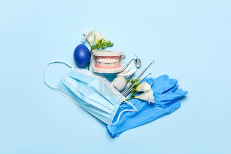 Dental tools with jaw model, flowers and Easter egg on blue background