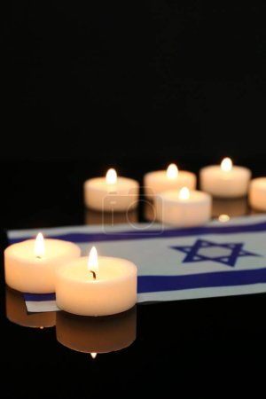 Burning candles with flag of Israel on dark background, closeup. International Holocaust Remembrance Day