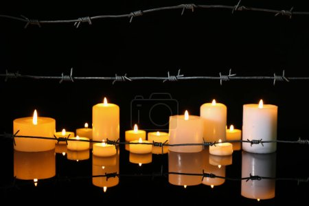 Téléchargez les photos : Fil barbelé et bougies allumées sur table en verre sur fond sombre. Journée internationale de commémoration de l'Holocauste - en image libre de droit