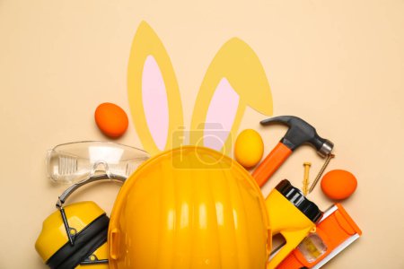 Photo for Builder's equipment with bunny ears and Easter eggs on beige background - Royalty Free Image