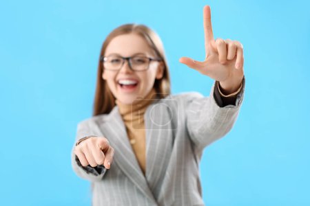 Photo for Young businesswoman showing loser gesture and pointing at viewer on blue background, closeup - Royalty Free Image