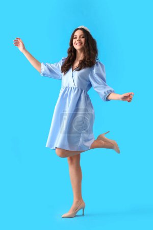 Teenage girl in tiara and prom dress dancing on blue background