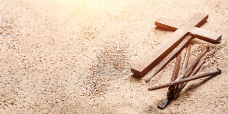 Wooden cross and nails on sand, closeup. Good Friday concept