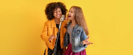 Photo for Teenage girls singing in microphone against yellow background - Royalty Free Image