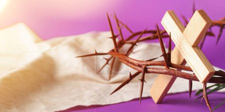 Foto de Crown of thorns, wooden cross and shroud on purple background, closeup. Good Friday concept - Imagen libre de derechos