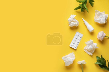 Nasal drops with pills, flowers and tissues on yellow background. Seasonal allergy concept