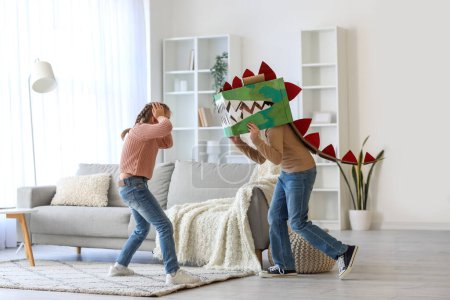 Verängstigtes kleines Mädchen und ihr Bruder im Dinosaurier-Kostüm aus Pappe zu Hause