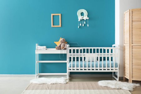 Photo for Comfortable baby crib and table with toy near blue wall - Royalty Free Image