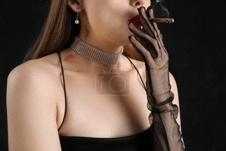 Foto de Hermosa joven con mordeduras de amor en su cuello fumar cigarrillo contra el fondo oscuro, primer plano - Imagen libre de derechos