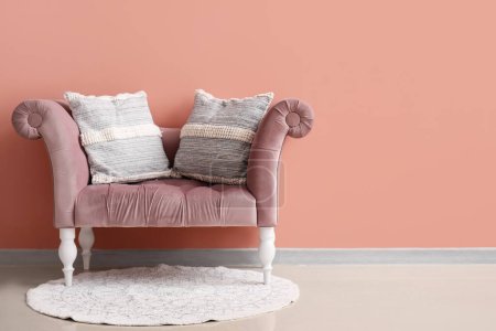 Foto de Elegantes almohadas decorativas en acogedor sillón cerca de la pared rosa - Imagen libre de derechos