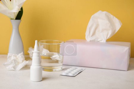 Photo for Nasal drops with pills, tissues, glass of water and flower on table near yellow wall. Seasonal allergy concept - Royalty Free Image