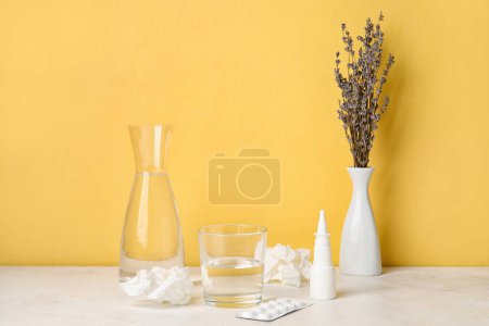 Photo for Nasal drops with pills, flowers, tissues and glass of water on table near yellow wall. Seasonal allergy concept - Royalty Free Image