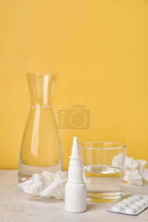 Photo for Nasal drops with pills, glass of water and tissues on table near yellow wall. Seasonal allergy concept - Royalty Free Image
