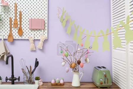 Téléchargez les photos : Vase avec branches de saule, œufs peints et guirlande de lapin dans la cuisine décorée pour la célébration de Pâques - en image libre de droit