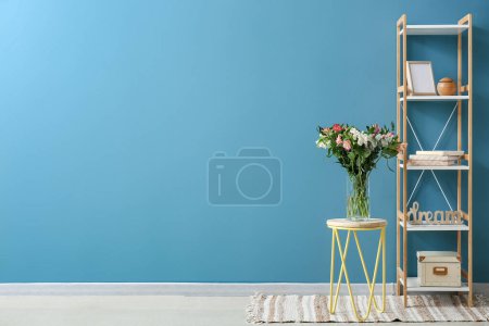 Foto de Florero con hermosas flores de alstroemeria en taburete y estantería cerca de la pared azul - Imagen libre de derechos