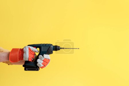 Téléchargez les photos : Travailleur avec perceuse électrique sur fond jaune - en image libre de droit