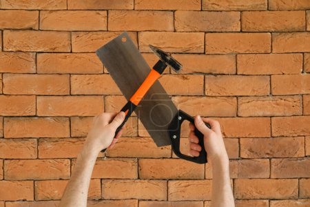 Téléchargez les photos : Travailleur avec marteau et scie à main sur fond de brique - en image libre de droit