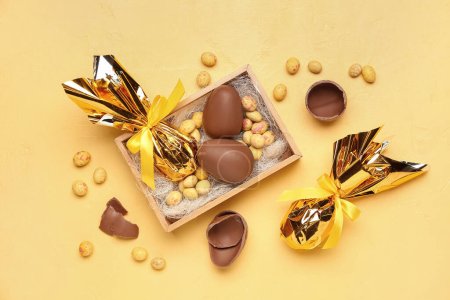 Téléchargez les photos : Boîte avec des œufs de Pâques en chocolat et des bonbons sur fond jaune - en image libre de droit