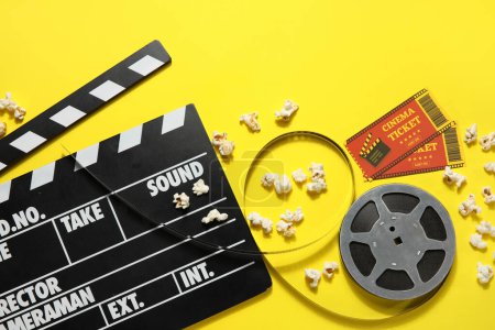 Foto de Película clapper con carrete, palomitas de maíz y entradas sobre fondo amarillo - Imagen libre de derechos