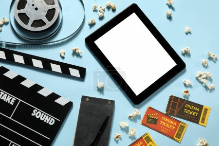 Téléchargez les photos : Film clapper avec bobine, pop-corn, tablette, billets et pop-corn sur fond bleu - en image libre de droit