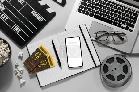 Téléchargez les photos : Movie clapper avec téléphone portable, ordinateur portable, bobine, lunettes et bloc-notes sur fond gris - en image libre de droit