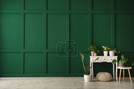 Foto de Mesas con plantas de interior y puf cerca de la pared verde en la habitación - Imagen libre de derechos