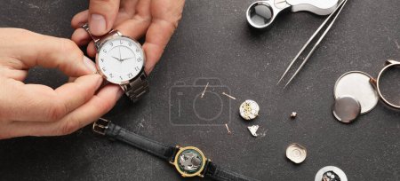 Clock maker's hands with broken watches and tools on dark background