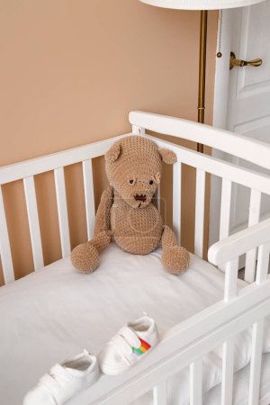 Foto de Cuna con oso de juguete y botines de bebé en el dormitorio, primer plano - Imagen libre de derechos