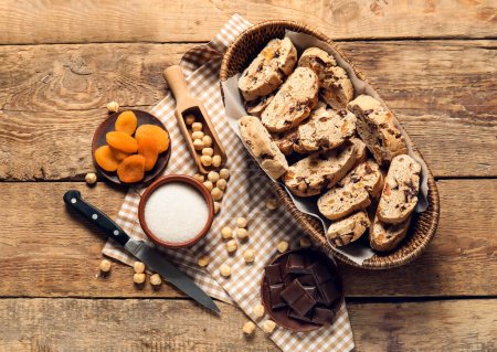 Basket with delicious biscotti cookies, chocolate, dried apricots and hazelnuts on wooden background