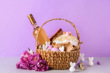 Photo for Basket with Easter eggs, cake, bottle of wine and tulip flowers on lilac background - Royalty Free Image