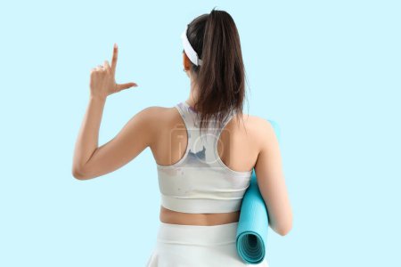Photo for Sporty young woman with mat showing loser gesture on blue background, back view - Royalty Free Image