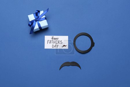 Téléchargez les photos : Composition avec monocle en papier, moustache, carte de voeux et cadeau pour la fête des pères sur fond de couleur - en image libre de droit