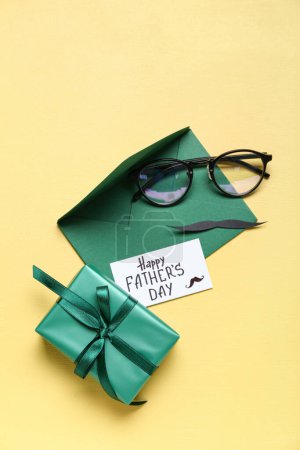 Téléchargez les photos : Papier avec texte JOURNÉE DU PÈRE, cadeau, enveloppe, moustache et lunettes sur fond jaune - en image libre de droit