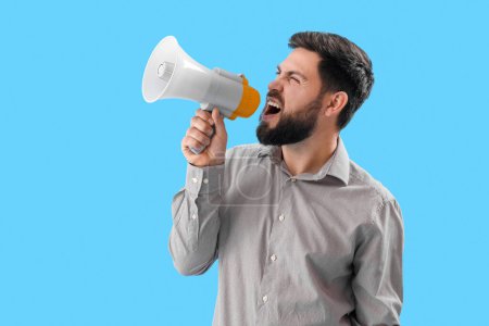 Téléchargez les photos : Jeune homme en colère criant en mégaphone sur fond bleu - en image libre de droit