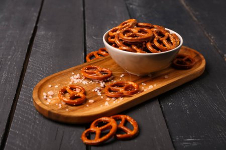 Photo for Board with bowl of tasty salted pretzels on dark wooden background - Royalty Free Image