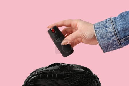 Woman putting pepper spray in bag on pink background, closeup
