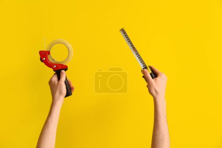 Téléchargez les photos : Travailleur avec adhésif et rubans à mesurer sur fond jaune - en image libre de droit