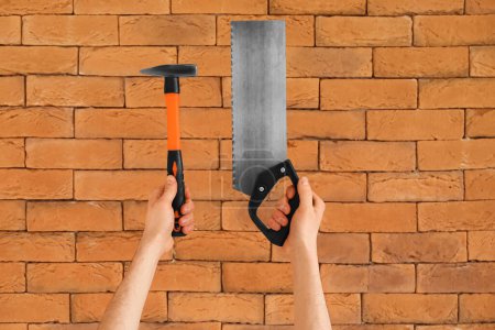 Téléchargez les photos : Travailleur avec marteau et scie à main sur fond de brique - en image libre de droit
