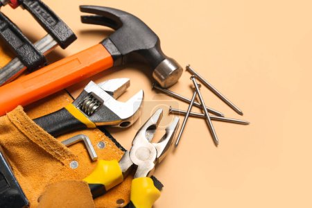Pliers in belt with tools on beige background