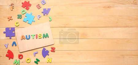 Word AUTISM, letters and puzzle pieces on wooden background with space for text